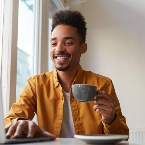 african-american-sitting-table-cafe-working-laptop-wears-yellow-shirt-drinks-aromatic-coffee-communicates-with-his-sister-which-is-far-another-country-enjoys-work 2 african-american-sitting-table-cafe-working-laptop-wears-yellow-shirt-drinks-aromatic-coffee-communicates-with-his-sister-which-is-far-another-country-enjoys-work 2